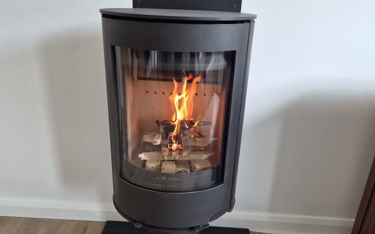 A curved free-standing stove on a granite hearth, fitted by Stove Fit, lit