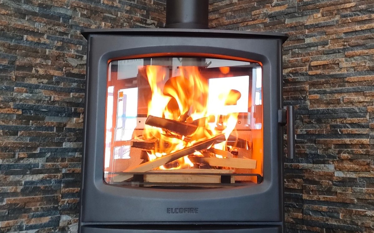 A wood burning stove on a log store stand against a split-face stone wall, fitted by Stove Fit